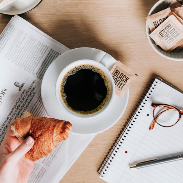 sort kaffe fra bryganlæg på avis med croissant og sukker