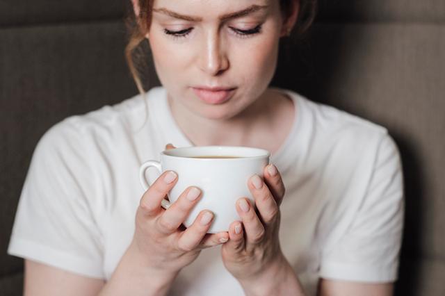 Kvinde i skjorte holder om en kop kaffe brygget på en bravilor bonamat kaffemaskine