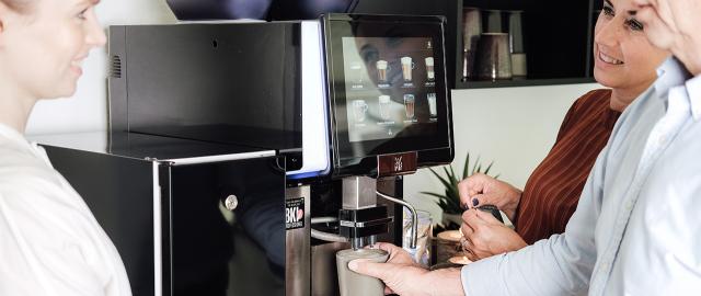 Kolleger taler ved kaffemaskinen om hvordan man kan spare på kaffeløsning