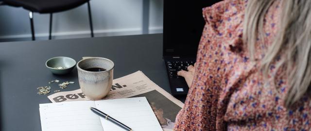 kvinde drikker firmakaffe foran computeren 